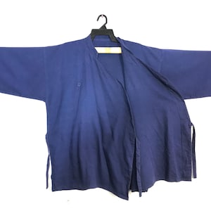 Peut inclure: Veste de style kimono bleu marine avec de larges manches, suspendue à un cintre noir. La veste est ouverte sur le devant et possède une fermeture à un seul bouton. Le tissu semble être du coton ou du lin léger.