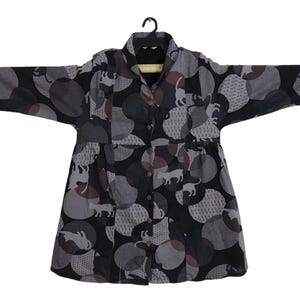 Könnte beinhalten: Ein langärmeliges, geknöpftes Kleid mit schwarzem Hintergrund und einem Muster aus weißen Kreisen mit grauen und braunen Tier-Silhouetten.