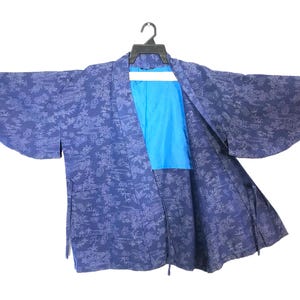 Puede incluir: Una bata azul marino estilo kimono con un estampado floral y un forro azul brillante. La bata está colgada de una percha negra sobre un fondo blanco. Las mangas son anchas y la bata está abierta.