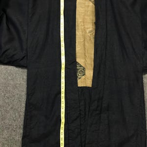 Puede incluir: Bata negra estilo kimono con un panel interior dorado y estampado. La bata se mide con una cinta m&eacute;trica amarilla, que muestra una longitud de aproximadamente 99 cm. La bata tiene una apariencia texturizada.