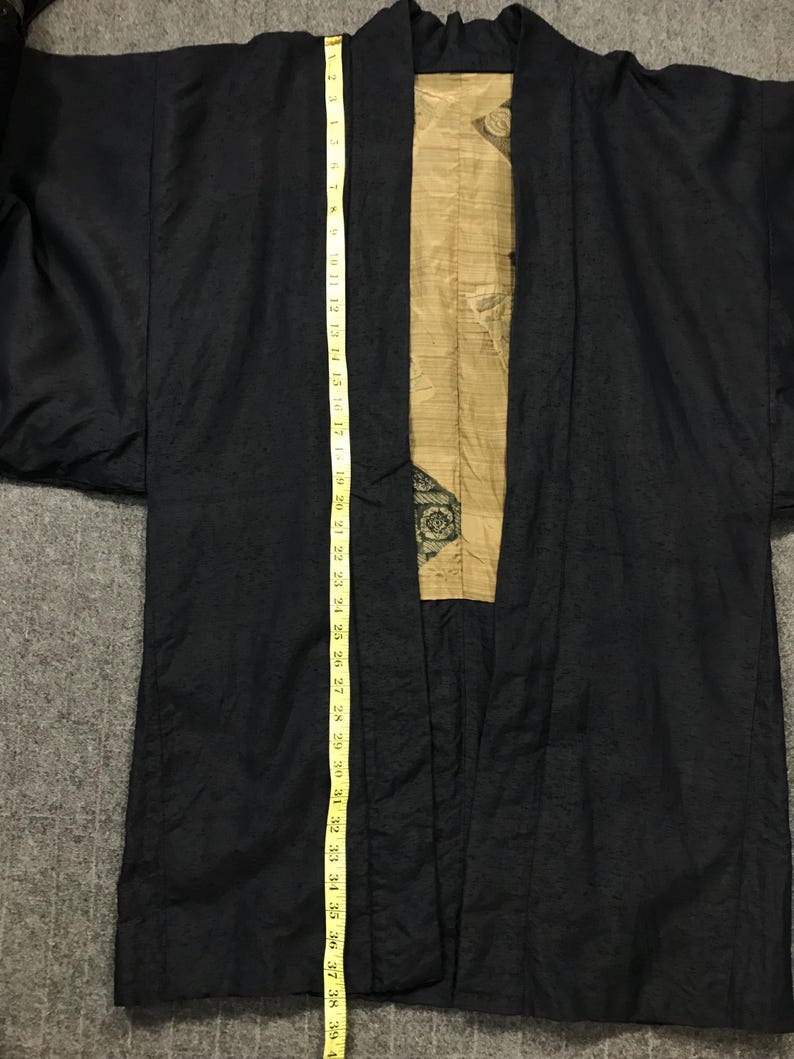 Puede incluir: Bata negra estilo kimono con un panel interior dorado y estampado. La bata se mide con una cinta m&eacute;trica amarilla, que muestra una longitud de aproximadamente 99 cm. La bata tiene una apariencia texturizada.