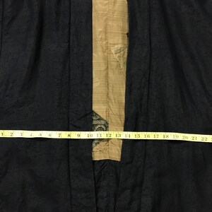 Puede incluir: Bata negra estilo kimono con un patr&oacute;n texturizado. Un panel beige recorre el centro, adornado con un dise&ntilde;o decorativo. Una cinta m&eacute;trica amarilla muestra el ancho de la bata, hasta 66 cm.