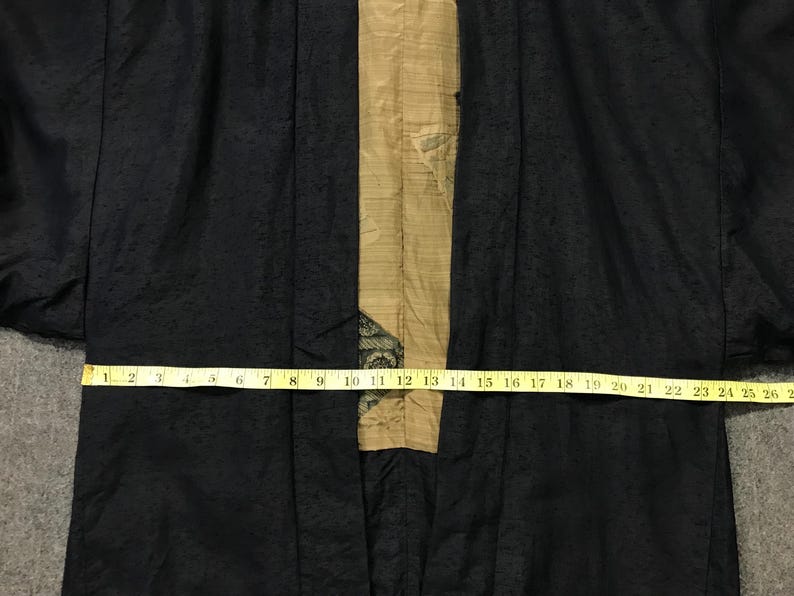 Puede incluir: Bata negra estilo kimono con un patr&oacute;n texturizado. Un panel beige recorre el centro, adornado con un dise&ntilde;o decorativo. Una cinta m&eacute;trica amarilla muestra el ancho de la bata, hasta 66 cm.