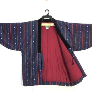 May include: A dark blue kimono-style jacket with vertical stripes in red, white, and blue. The jacket has a black velvet collar and a red interior lining. The sleeves are wide and the jacket is hanging on a black hanger.