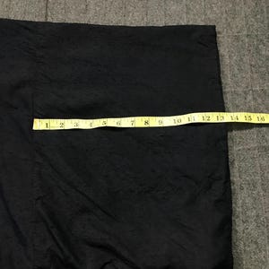 Puede incluir: Prenda negra con superficie texturizada, posiblemente una chaqueta o kimono. Una cinta m&eacute;trica amarilla est&aacute; colocada sobre la tela, mostrando una longitud de aproximadamente 40 cm. El fondo es una superficie gris texturizada.