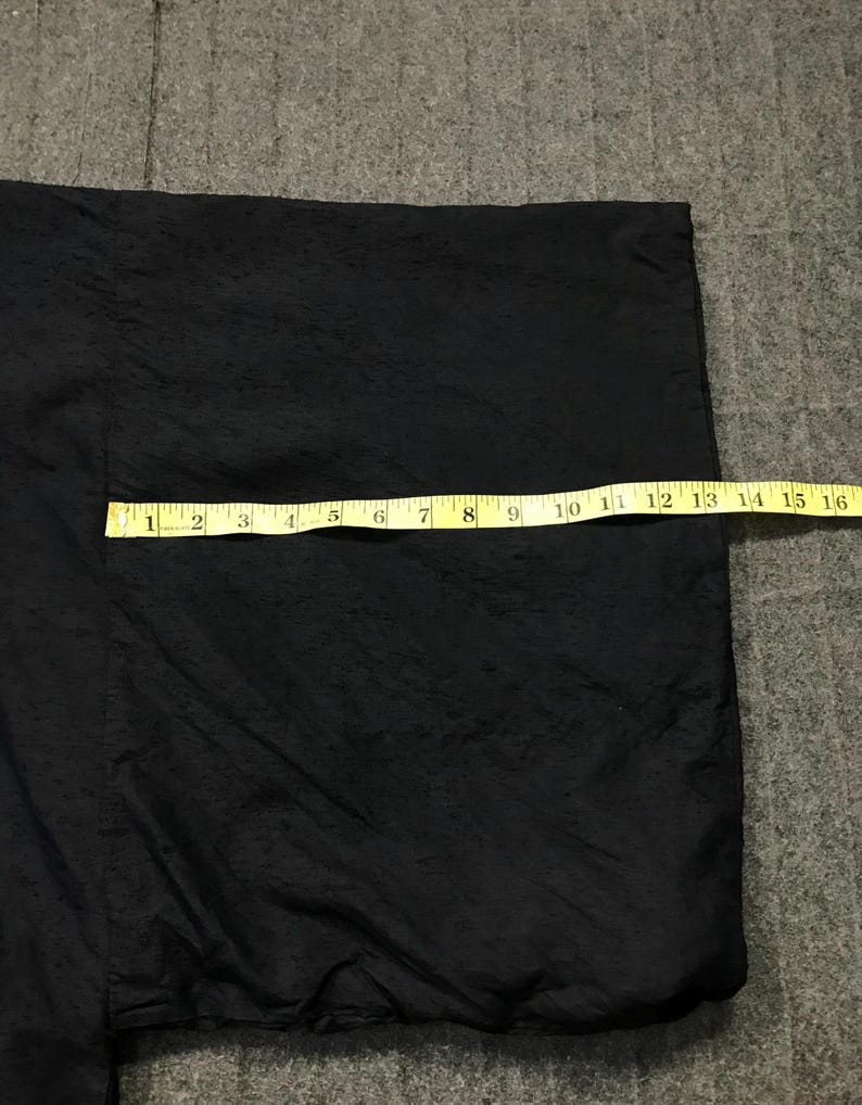 Puede incluir: Prenda negra con superficie texturizada, posiblemente una chaqueta o kimono. Una cinta m&eacute;trica amarilla est&aacute; colocada sobre la tela, mostrando una longitud de aproximadamente 40 cm. El fondo es una superficie gris texturizada.