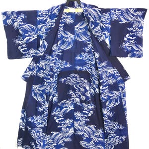 May include: A dark blue kimono featuring a repeating white graphic pattern of stylized ocean waves. The garment has wide sleeves, an open front design, and a straight hemline, displaying a consistent wave motif across the entire fabric surface.