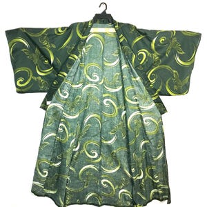 May include: A dark green kimono featuring a repeating pattern of light green and yellow stylised birds and swirling circular motifs. The garment has wide sleeves, an open front, and is displayed on a black plastic hanger against a white background.