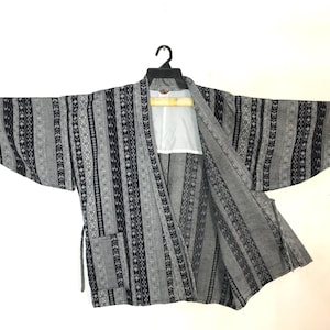 May include: A gray and black patterned kimono-style jacket with long sleeves, hanging on a black hanger. The jacket features a vertical stripe design with geometric and floral motifs. The interior is white.