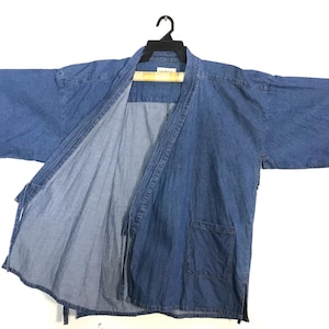 May include: A blue denim kimono jacket with wide sleeves and a relaxed fit. The jacket has an open front, a small pocket on the front, and a tie closure. The garment is hanging on a black hanger.