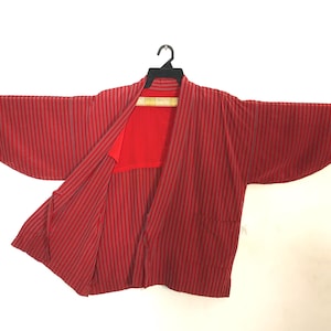 May include: Red and gray striped kimono-style jacket hanging on a black hanger. The jacket has wide sleeves and a red interior. The fabric has a vertical stripe pattern. The garment is displayed against a white background.