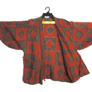 May include: A red and brown patterned kimono-style jacket with a diamond design. The jacket is hanging on a black hanger against a white background. The sleeves are wide and the fabric appears textured.