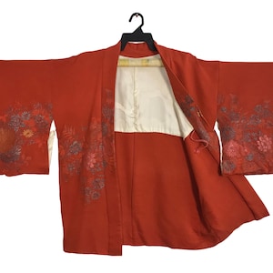 Puede incluir: Un kimono rojo con bordados florales. El kimono está abierto para revelar un forro blanco. El kimono está hecho de una tela suave y ligera.