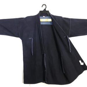 May include: A dark navy blue kimono-style jacket with long sleeves, hanging on a black hanger. The jacket has a wrap-around design with a contrasting light blue and yellow panel visible at the neckline. It features tie closures and a relaxed fit.