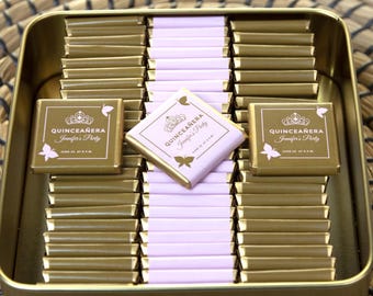 Puede incluir: Una lata dorada llena de chocolates envueltos individualmente. Cada chocolate está envuelto en papel de aluminio dorado con un acento rosa. Los chocolates están decorados con una mariposa rosa y el texto "QUINCEAÑERA Jennifer's Party".