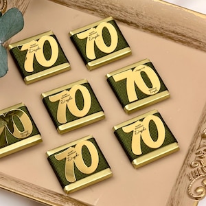 May include: A collection of chocolate bars arranged on a gold-colored tray. Each bar is wrapped in dark green paper and features a gold foil design with the number "70" and the text "Happy Birthday Daphne".