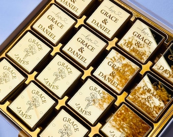 Op de afbeelding: Een witte doos gevuld met gouden chocoladevierkanten. Elk vierkant heeft een gepersonaliseerd bericht met de namen "Grace & Daniel" of "Grace & James" en het woord "love" met een hartje.