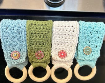 May include: Four crocheted pot holders with wooden rings. The pot holders are in blue, green, white, and light blue. Each pot holder has a decorative button in the center.