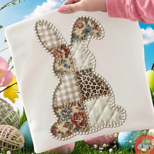 May include: A white square pillow with a patchwork bunny design. The bunny is made of various fabrics, including floral, gingham, and leopard print, and is outlined with small white beads. The pillow is held against a background of grass, Easter eggs, and a blue sky.