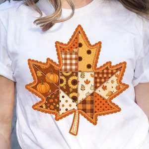 Könnte beinhalten: Weißes T-Shirt mit einem großen Ahornblatt-Design im Patchwork-Stil. Das Blatt enthält Herbstmuster wie Kürbisse, Sonnenblumen und Karomuster in Orange-, Braun- und Gelbtönen. Das Blatt hat einen gezackten Rand.