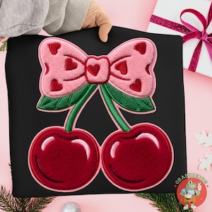 Può includere: Felpa nera con un disegno ricamato di due ciliegie e un fiocco rosa. Le ciliegie sono di un rosso intenso e il fiocco è decorato con piccoli cuori rossi. Il disegno ha foglie verdi.