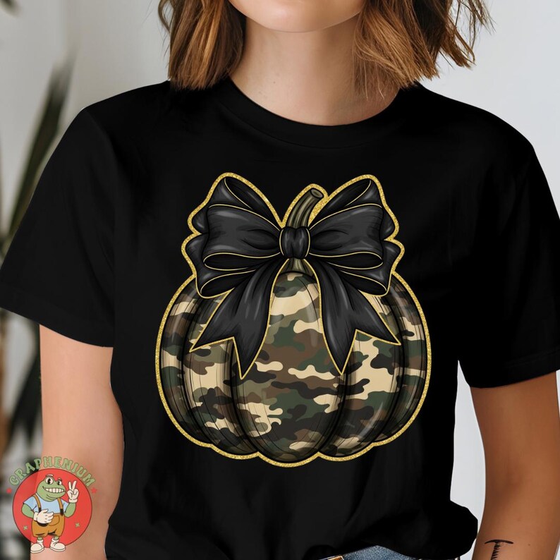 May include: Black t-shirt featuring a camouflage pumpkin design with a large black bow. The pumpkin has a gold outline. The design is centered on the shirt, creating a festive and stylish look.