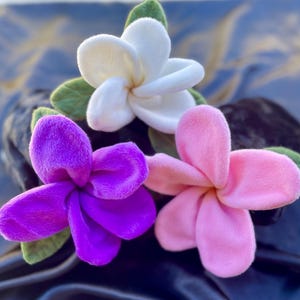 May include: Three fabric flowers in white, pink, and purple. The flowers are made of soft, plush fabric and have a realistic appearance.