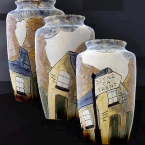 Può includere: Tre vasi in ceramica con un designo dipinto a mano di case e un cartello stradale che recita "Stoke on Trent". I vasi sono smaltati in tonalità di marrone, blu e bianco.