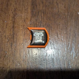 May include: Orange plastic game piece with a black and white cow design.