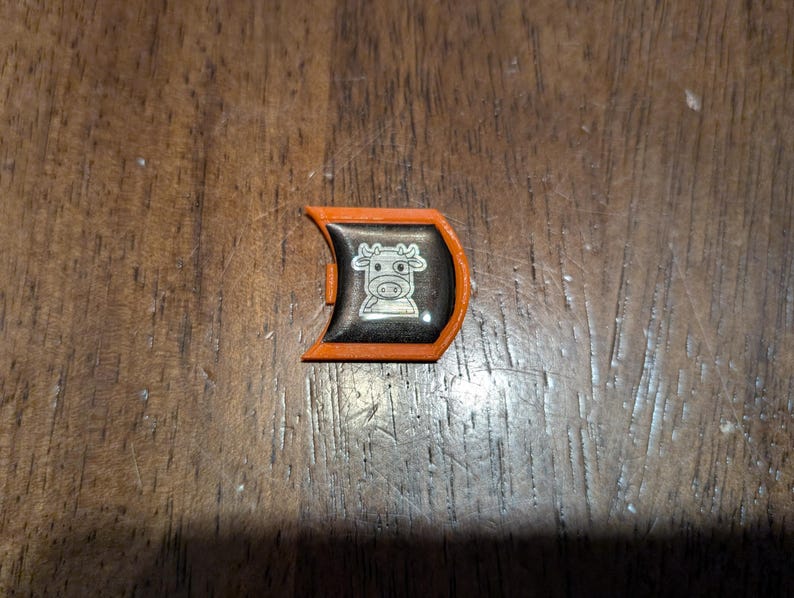 May include: Orange plastic game piece with a black and white cow design.