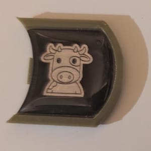 May include: A green plastic keychain with a black and white cartoon cow design.