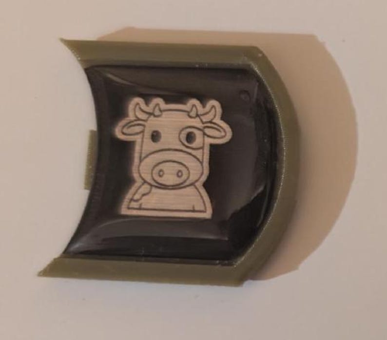 May include: A green plastic keychain with a black and white cartoon cow design.