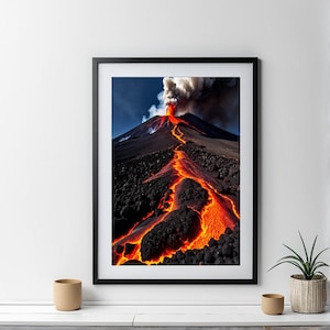 Puede incluir: Una impresión enmarcada que muestra una erupción volcánica. La imagen captura una montaña con una superficie oscura y rocosa, y un río de lava naranja brillante que fluye por su lado. Humo blanco sale de la cima del volcán contra un cielo azul.