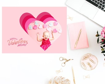 May include: A pink card with a layered heart design featuring a baby girl smiling and holding up her arms. The text "Happy Valentines Day" is written in pink letters on the card.