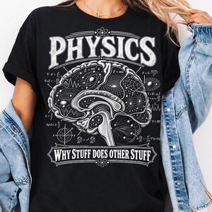 Puede incluir: Una camiseta negra de manga corta con un gráfico blanco de un cerebro humano lleno de ecuaciones de física y patrones celestiales. El texto PHYSICS está impreso sobre el cerebro y WHY STUFF DOES OTHER STUFF debajo.