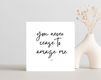 May include: A white card with black calligraphy that reads "you never cease to amaze me" with a small pink heart at the bottom.