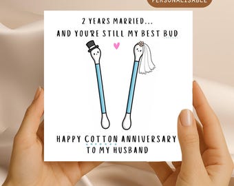 May include: A square greeting card featuring two cartoon cotton swabs with faces. One wears a black top hat, the other a white veil. Text reads: 2 YEARS MARRIED... AND YOU'RE STILL MY BEST BUD. HAPPY COTTON ANNIVERSARY TO MY HUSBAND.
