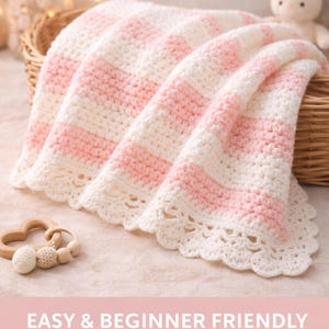 Op de afbeelding: Een handgemaakte babydeken met roze en witte strepen, gepresenteerd in een rieten mand. De deken heeft een crèmekleurige geschulpte rand. De tekst "EASY & BEGINNER FRIENDLY" is zichtbaar. Een houten speelgoed en een pluchen konijn staan ook in de afbeelding.