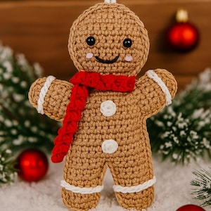 以下が含まれることがあります： かぎ針編みのジンジャーブレッドマンのクリスマスオーナメント。オーナメントはタン色で、白いアクセント、赤いスカーフ、黒い目があります。ジンジャーブレッドマンは笑顔で、白いボタンで飾られています。