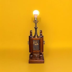 May include: A wooden table lamp with a brass base and a clear glass shade. The lamp has a caged design and a light bulb is turned on.