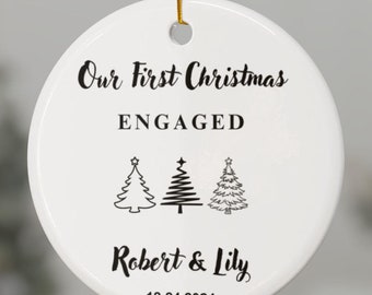 Może przedstawiać: Biała ceramiczna ozdoba choinkowa z czarnym tekstem "Our First Christmas ENGAGED Robert & Lily 12.24.2024" i trzema stylizowanymi choinkami.