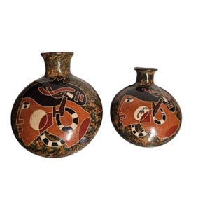 May include: Two ceramic vases with a black, brown, red, and white geometric design featuring stylized human faces. The vases are round and have a speckled glaze.