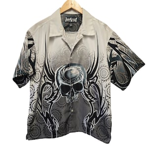 May include: A button-down short-sleeve shirt with a skull graphic. The shirt features a gray and black skull design on a light gray background. The sleeves and background have a spiral pattern.