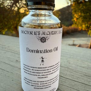 Pode incluir: Uma garrafa de vidro transparente com um rótulo branco que diz "Domination Oil" e instruções de uso. O rótulo também inclui o texto "Doctor B's Alchemy, LLC".