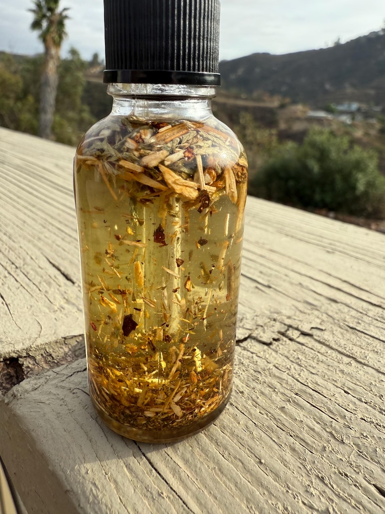 May include: A clear glass bottle with a black lid filled with a golden liquid and various herbs and botanicals. The bottle is sitting on a wooden surface.