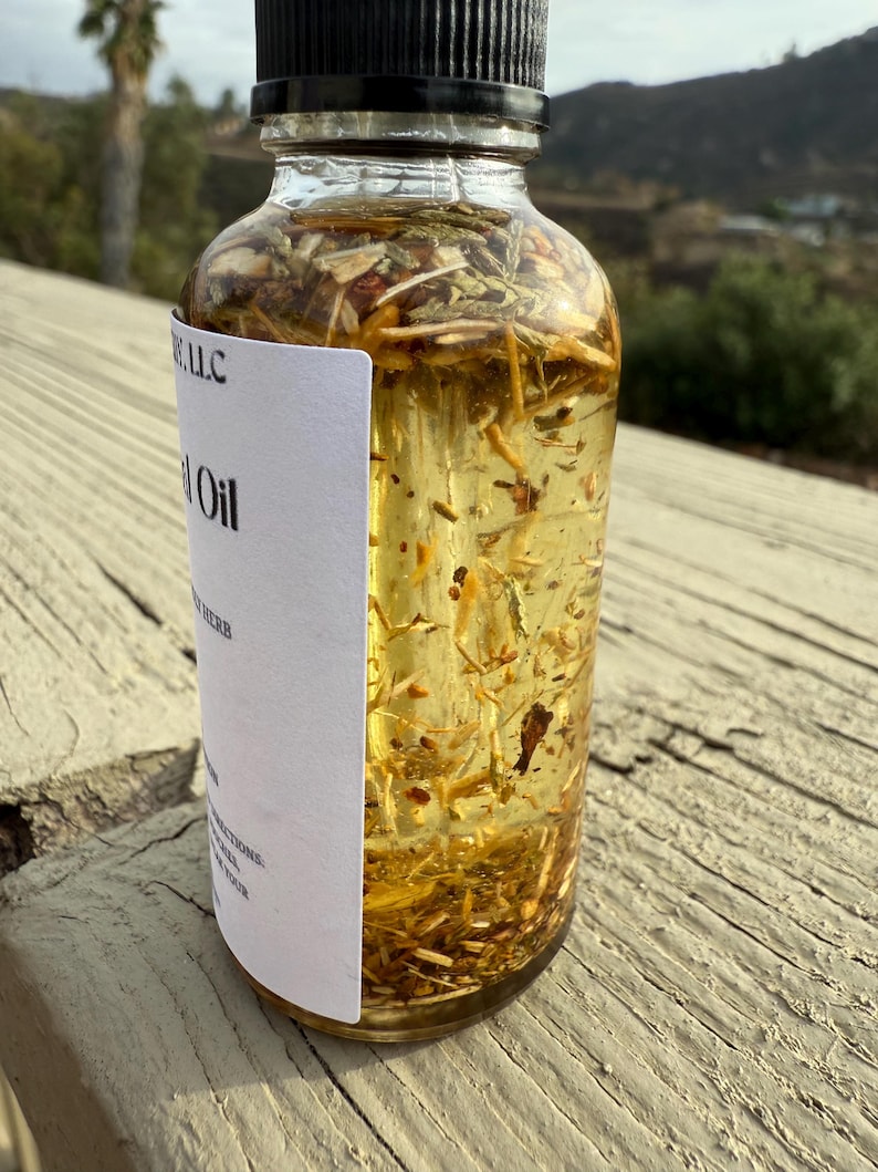 May include: A clear glass bottle with a black cap filled with a yellow liquid and herbs. The label on the bottle reads "Herb Oil" and "[Company Name] LLC".