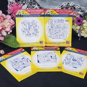 Op de afbeelding: Verschillende pakketten Aunt Martha's strijktransfers voor borduren, textielschilderen en quilten. De gele verpakkingen met rode en blauwe tekst tonen diverse ontwerpen, waaronder schattige muizen en andere patronen.