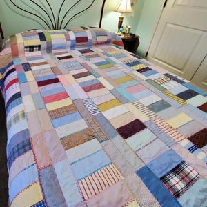 May include: A patchwork quilt in a variety of pastel colors, including blue, pink, yellow, and white, covers a bed. The quilt is made of rectangular fabric pieces sewn together. The bed has a decorative metal headboard.