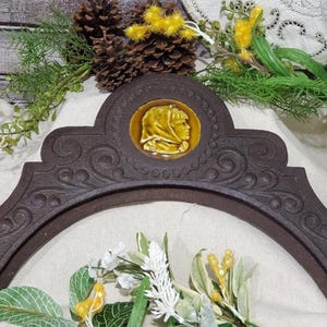 Può includere: Un elemento decorativo ad arco marrone scuro con un medaglione ovale dai toni gialli raffigurante un profilo. Il pezzo presenta volute ornate e una forma curva, forse per un camino o una decorazione murale.