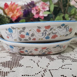 May include: A white ceramic mug with a black handle and the text "But First, Coffee" in a bold, black font. The mug is set against a blurred background. The mug appears to be approximately 10 cm tall.